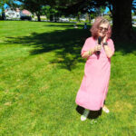 essa who is wearing a pink dress is standing on the green at Mt Albert War Memorial Park. She has a microphone in her hand.